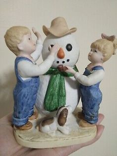 a hand holding a figurine of two children and a snowman