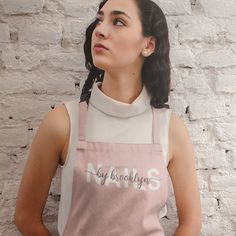 a woman wearing an apron with the words brooklyn on it, standing in front of a brick wall