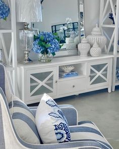 a living room filled with furniture and blue flowers on top of a white shelf next to a mirror