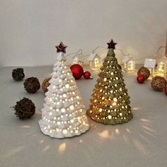 three small christmas trees with lights on them and some ornaments around them, all in different shapes and sizes