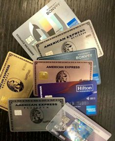 several credit cards stacked on top of each other in front of a wooden table with the words american express written on it