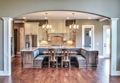 a large open concept kitchen and dining room with hardwood floors, white cabinets and an archway leading to the living room