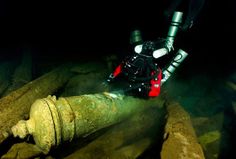 a scuba is submerged in the water next to a large piece of wood and pipes