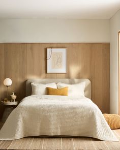 a bed with white sheets and pillows in a bedroom next to a lamp on a table