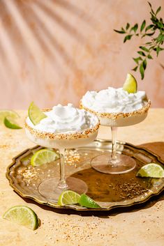 two margarita cocktails with lime wedges and whipped cream on a serving platter