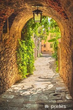 an alley way with stone walls and cobblestone pavement leading to a street lamp