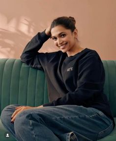 a woman sitting on top of a green couch smiling at the camera with her hands behind her head