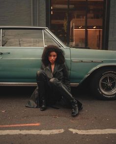 a woman sitting on the ground next to a car