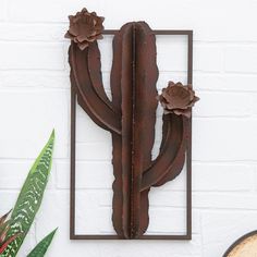 a metal cactus with three flowers mounted to the side of a white brick wall next to a potted plant