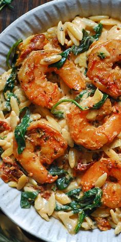 pasta with shrimp and spinach in a white bowl on top of a wooden table