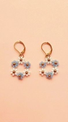 two small blue and white beads are hanging from gold hoop earrings on a pink background