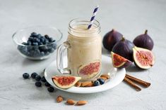 a glass mug filled with smoothie next to sliced figs and blueberries on a plate