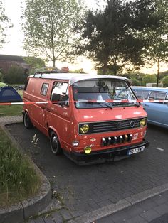 an orange van parked next to other cars in a parking lot with trees and grass