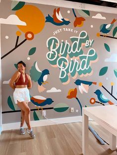 a woman standing in front of a wall with birds on it and the words just take it bird by bird