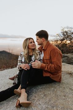 a man and woman sitting on top of a rock