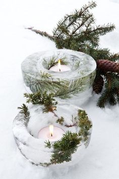 two candles are sitting in the snow next to pine cones