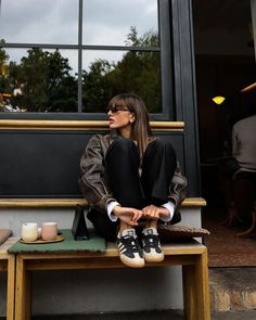 a woman sitting on top of a wooden bench next to a cup and saucer