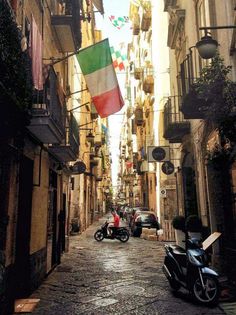 an italian flag is flying in the air over a narrow alleyway between two buildings