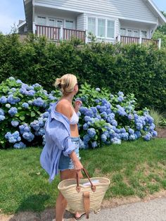 a woman is walking down the street carrying a wicker basket in front of blue hydrangeas