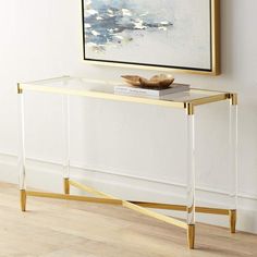 a glass and gold console table in front of a painting