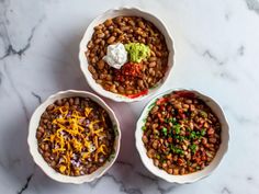 three bowls filled with beans and cheese on top of a marble countertop next to another bowl