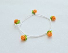 an orange and green beaded bracelet on a white string with two small beads attached to it