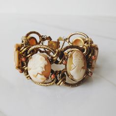 This vintage cameo bracelet is gorgeous! It features six carving blush pink shell carved cameos set in gold toned metal with decorative rope links and coral stones throughout. This set will make a wonderful and special holiday gift to yourself or a special friend.  --------------------------------------------------------------------------------------- Era: 1960s (Victorian style)  Best fits: fits most sizes Bracelet: width: 1/2 inches length: 7 1/2 inches Maker markings / Label: n/a Condition: E Vintage Adjustable Cameo Jewelry, Vintage Adjustable Cameo Bracelet, Adjustable Vintage Cameo Bracelet, Vintage Cameo Bracelet Jewelry, Vintage Cameo Bracelet, Cameo Bracelet, Vintage Cameo, Coral Stone, Vintage Bracelet