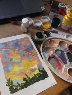 an artist's palette with paint and watercolors on it next to a laptop