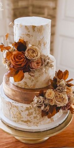 a three tiered wedding cake with flowers on the side and gold ribbon around it