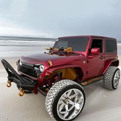 a red jeep parked on top of a sandy beach