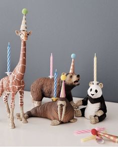 three toy animals with birthday hats and candles in front of one animal sitting on the ground