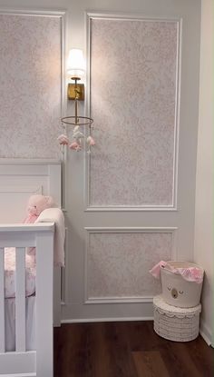 a baby's room with pink and white wallpaper, crib and lamp