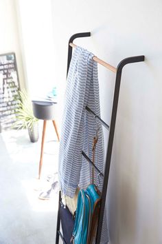 a coat rack with umbrellas hanging on it next to a white wall and potted plant