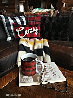 a plaid blanket, coffee mug and eyeglasses sit on a table in front of a couch