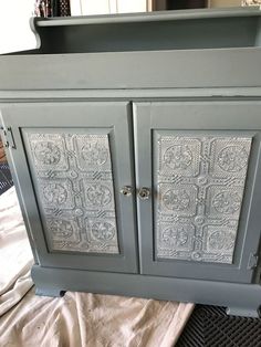 an old gray cabinet is being painted with metallic paint and decorative glass inserts on the doors