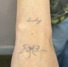 a woman's arm with a bow tattoo on it that says lovebug