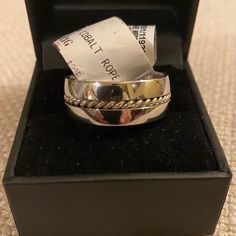 a silver ring in a black box on a carpeted floor with a ticket sticking out of it