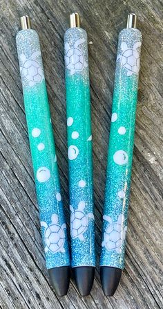 three pens sitting on top of a wooden table covered in blue and green glitters