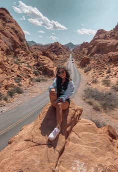 a woman sitting on top of a large rock next to a desert road with mountains in the background