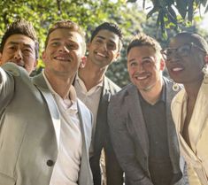 a group of men standing next to each other taking a selfie with their hands in the air