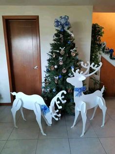 two white reindeer statues standing next to a christmas tree