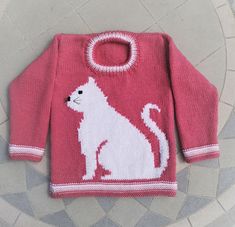 a knitted sweater with a cat on the front and bottom, sitting on a tile floor