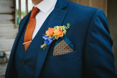 a man in a blue suit with an orange tie and flower boutonniere