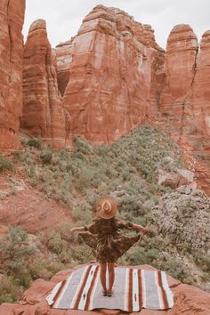 a woman standing on top of a blanket in front of red rocks and green trees