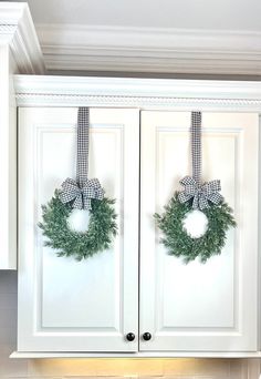 two wreaths hanging from the front of white cabinets