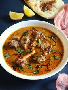 a bowl of soup with meat and vegetables in it next to some pita bread