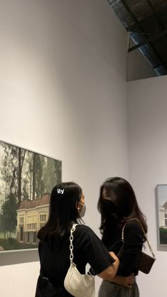 two women standing in front of a painting looking at each other's reflection on the wall