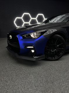 the front end of a blue sports car in a dark room with hexagonal lights