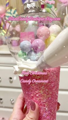 someone is holding up a pink cup filled with candies and gummy balls in front of a christmas ornament