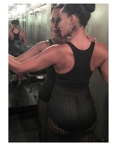 a woman in a black dress is looking at herself in the mirror and her back turned to the camera